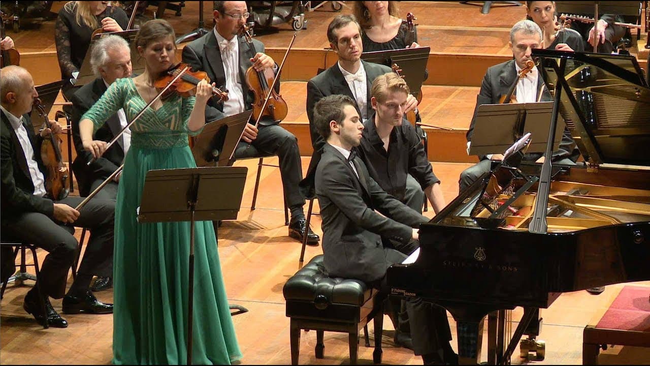 Soliste violoniste robe verte et pianiste devant orchestre symphonique